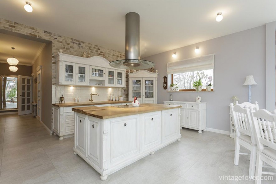 This minimalist kitchen is spacious and functional: high ceilings, a large center island, and bright white cabinets, furniture, and floors. The patterned wall-tiles provide a nice off set to the classic white of the room.