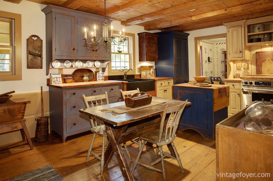 This kitchen is full of interesting colors and textures that delight the eye: a rustic, wooden table; blue cabinet and island; wooden floors and matching wooden ceilings. 