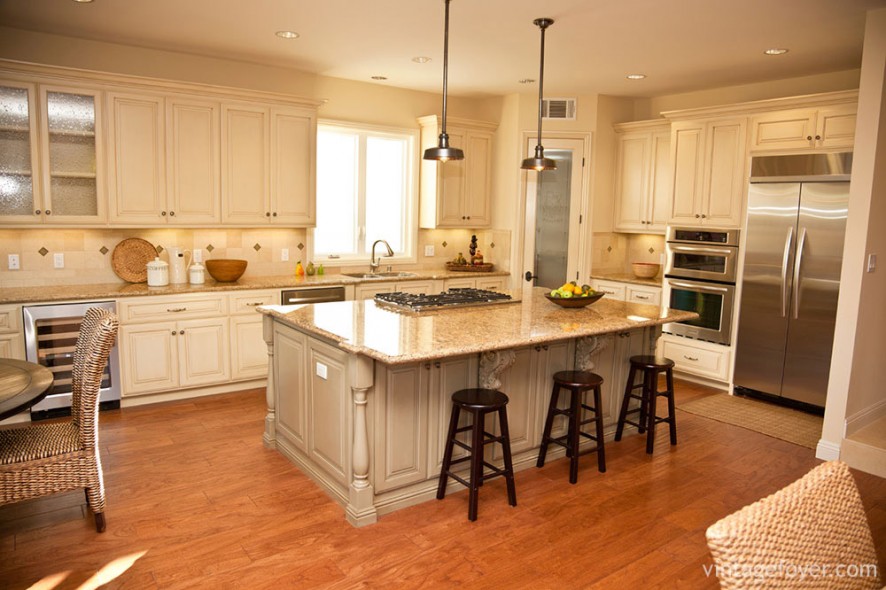 The cream, paneled cabinets of this kitchen are soft and welcoming, accented by the dark, wooden bar stools and hanging pendant light fixtures.