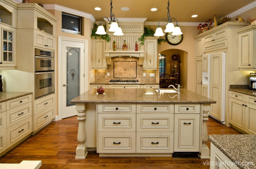 The elegance of this kitchen comes from the variety of colors and textures: cottage-style doors; the metal fixtures on the cabinets; the busy design of the marble countertops; and the hanging three-piece light fixtures. 