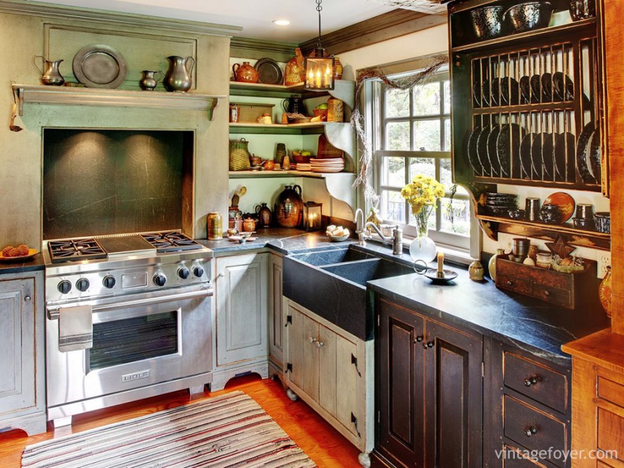 Busy, colorful, and cozy, this kitchen is full of character: exposed racks for plates and cups, differently stained wood cabinets, vintage green walls, and a striped floor mat. 