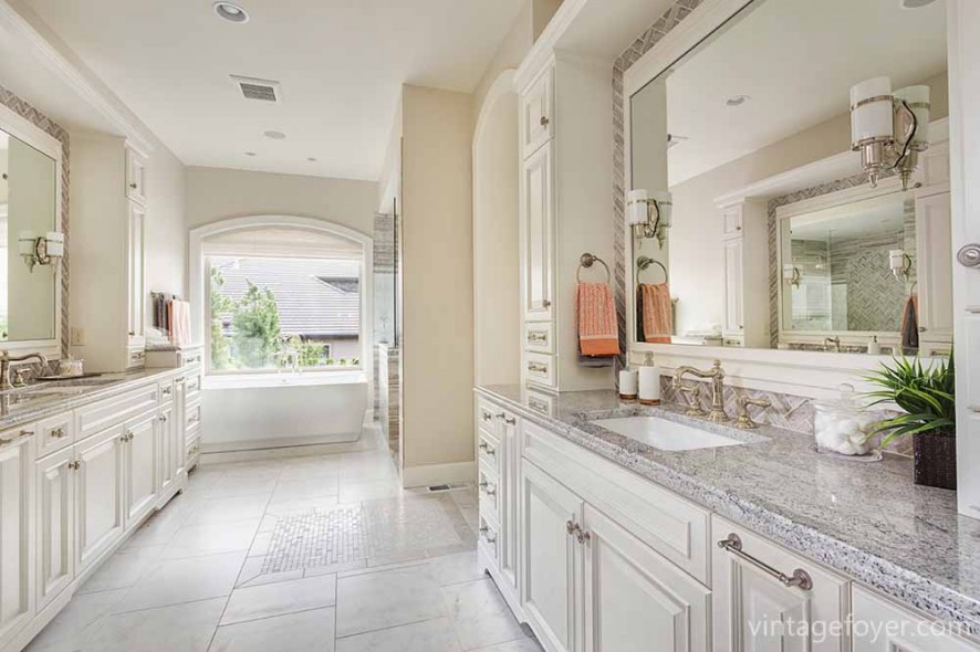 Large bathroom in luxury home with two sinks, tile floors, fancy cabinets, large mirrors, and bathtub
