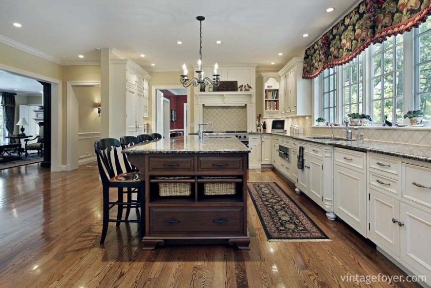 Medium toned hardwood flooring, dark toned island, and white custom cabinetry with matching black speckled marble countertops. 