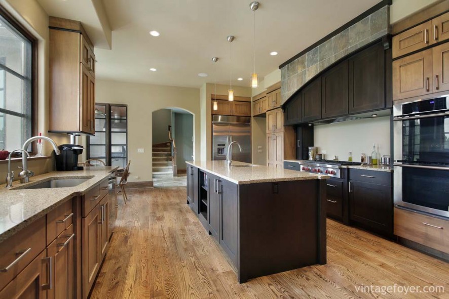 Custom dark toned cabinetry mixed with light toned shaker cabinets, light hardwood flooring, and tan speckled marble countertops. 