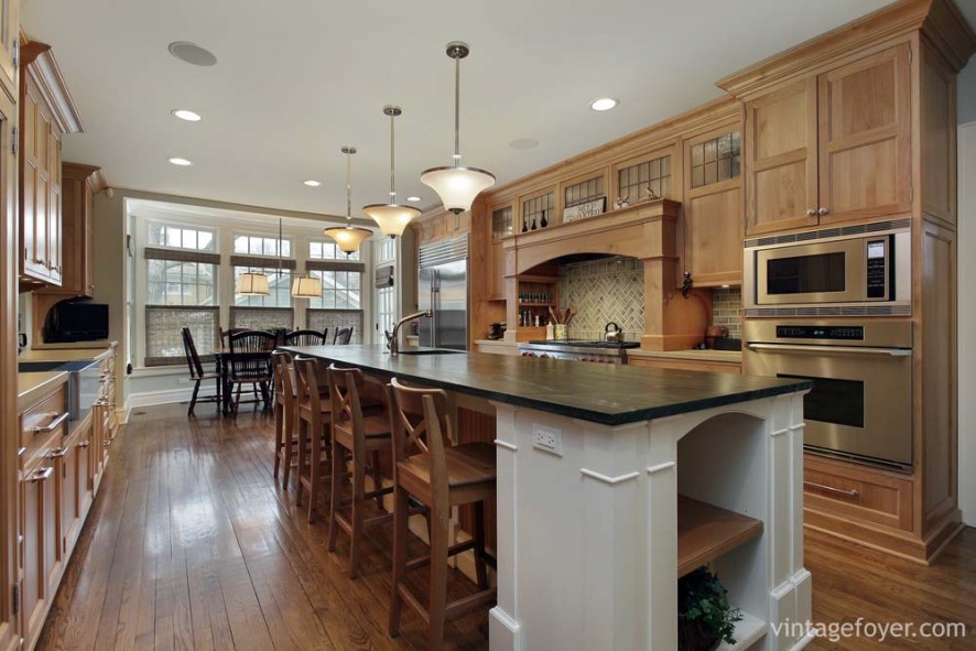 Medium toned shaker cabinets, white custom island and bar, quartz countertop on island, high end stainless steel appliances, and custom herringbone backsplash. 