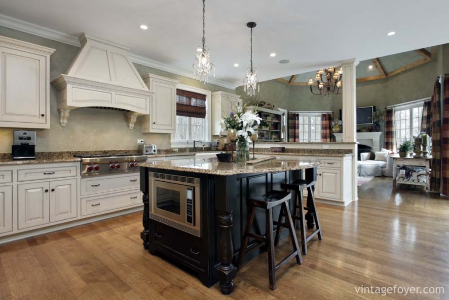 Custom white cabinetry and oven hood, beautiful tan speckled marble countertops, and a contrasting black island.