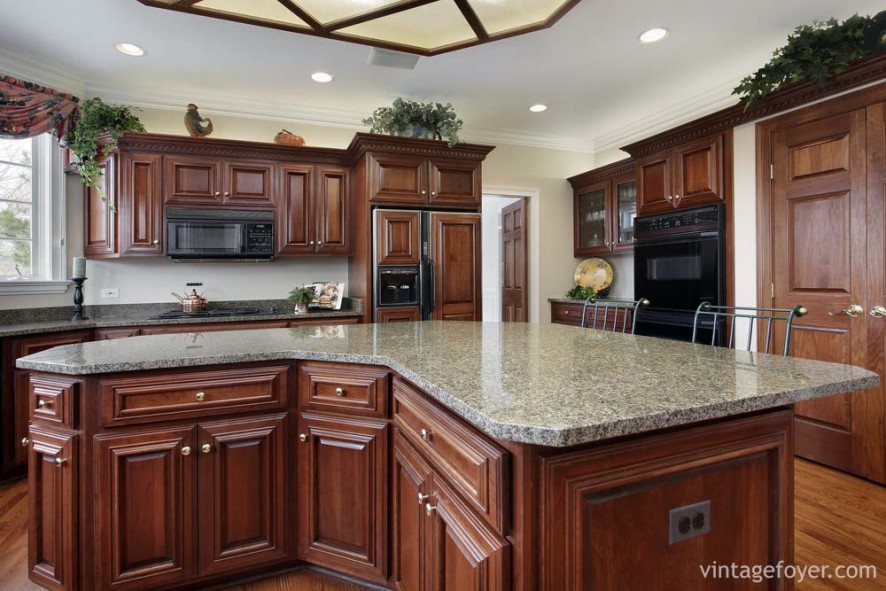 Beautiful custom cherry island and cabinetry, high end appliances with custom wood facings, black/grey speckled countertops, and light toned hardwood flooring. 
