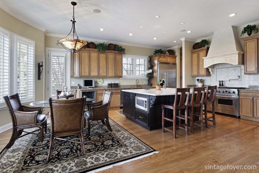 Black island with white marble countertop, custom traditional light toned cabinetry, high end stainless steel appliances, and beautiful tan speckled marble countertops. 