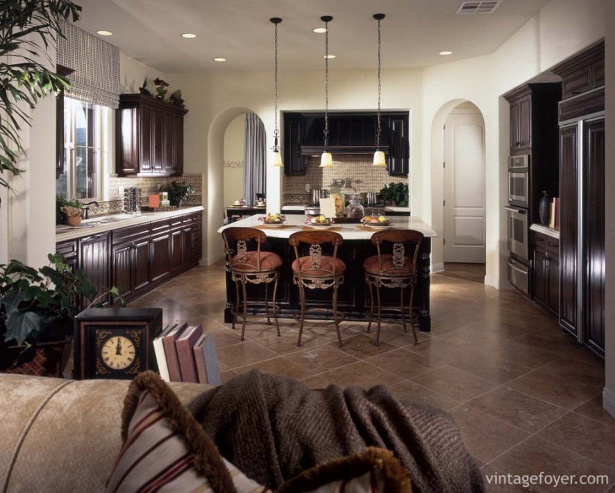 Large open kitchen with dark toned hardwood cabinetry, white quartz countertops, and tan toned porcelain tile flooring. 