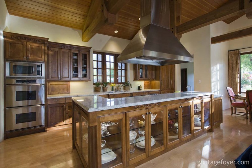 Traditional style dark toned cabinetry with architectural accents, Beautiful clear glass doors on the island, and white swirled marble countertops.