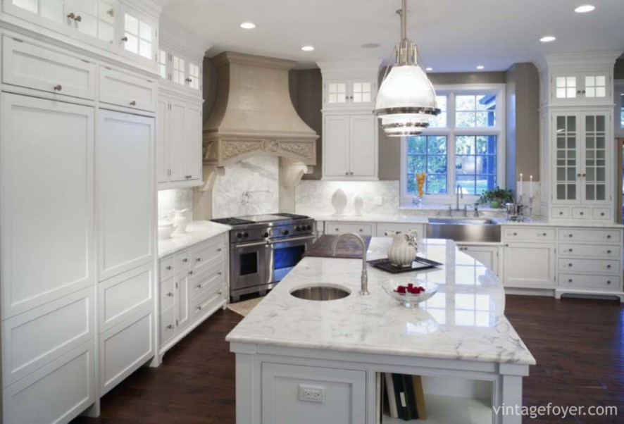 Luxurious white marble residential kitchen with hardwood floors, stainless steel appliances, and white enamel custom cabinets.