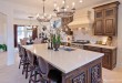 Custom designed island and cabinetry with white quartz countertops, custom oven hood with beautiful architectural details, elegant cream toned porcelain tile flooring.