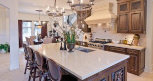 Custom designed island and cabinetry with white quartz countertops, custom oven hood with beautiful architectural details, elegant cream toned porcelain tile flooring.