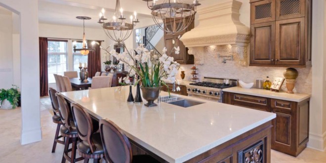 Custom designed island and cabinetry with white quartz countertops, custom oven hood with beautiful architectural details, elegant cream toned porcelain tile flooring.